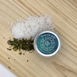 tin of seaweed salt on a wooden board with salt and dried seaweeds